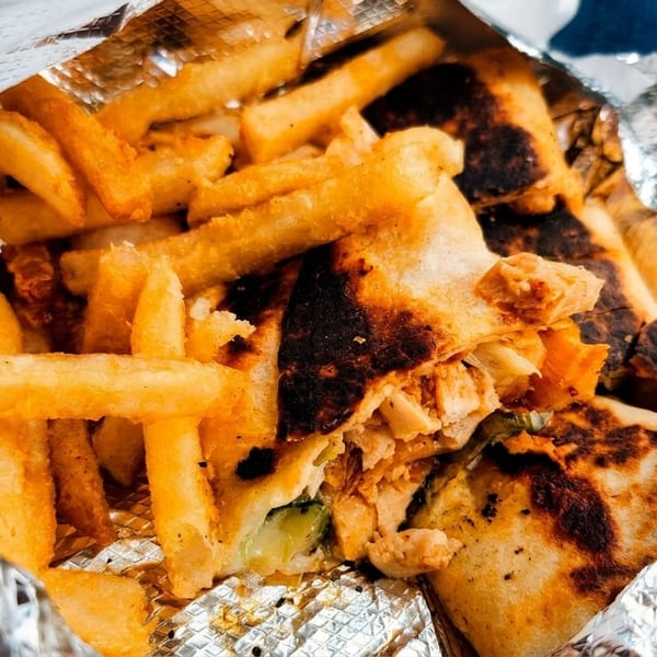 Crispy golden french fries and a grilled chicken wrap with charred edges in foil packaging.