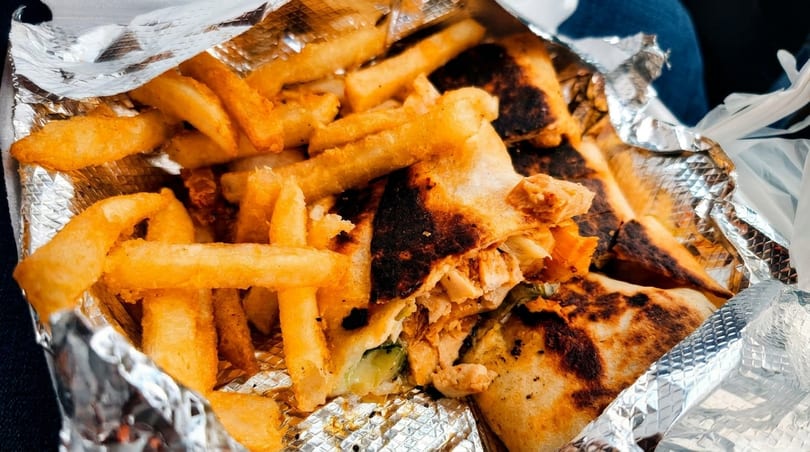 Crispy golden french fries and a grilled chicken wrap with charred edges in foil packaging.