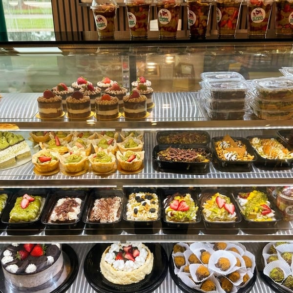 A brightly lit display case filled with various cakes, pastries, and desserts.