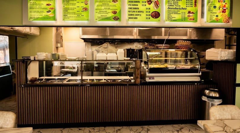 A restaurant counter with food warmers, a display case, and menu boards above.